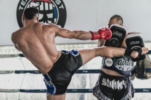 Dynamic action shot of two men sparring in Muay Thai kickboxing training inside a gym.