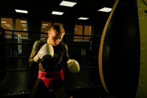 Focused male boxer training with a heavy bag in a dimly lit gym, showcasing intensity and skill.