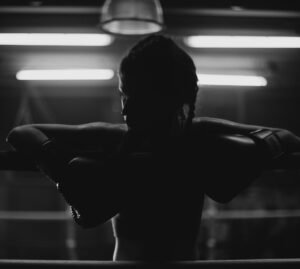 Monochrome image of a female boxer resting on the ropes in a dimly lit gym.