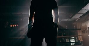 Silhouette of a boxer in a gym, illuminated by dramatic beams of sunlight, creating a powerful visual impact.
